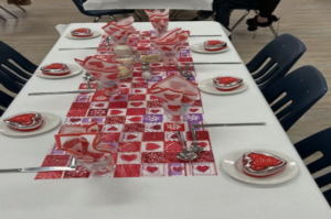 a table set with a white cloth and decorations for Valentine's Day
